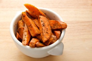 A cup of roasted sweet potatoes on a wooden table.