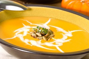 A bowl of creamy pumpkin soup topped with pumpkin seeds.