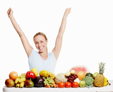 A happy women with her arms raised behind a selection of healthy foods.