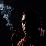 A man smoking on against a dark background.