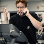 A man on an exercise bike and talking on his cell phone at the same time.