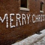 Merry Christmas written in snow on a brick wall.