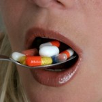 A woman eating a spoon full of vitamin pills.