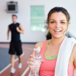 A woman in the gym drinking a bottle of water.