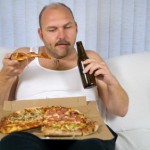 An overweight man drinking beer and eating pizza.
