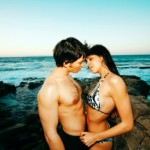 A young couple standing on the rocks near the sea.