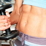 A woman with toned abs holding a dumbell.