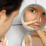 A woman with a spot examining it in the mirror.