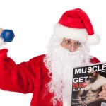 Santa lifting a dumbbell and reading a muscle building magazine.