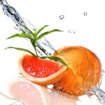 A sliced and whole grapefruit being splashed with water.