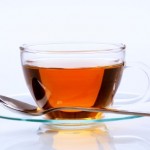 A glass cup of black tea on a glass saucer.