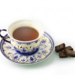 A cup of black tea and a saucer next to some dark chocolate chunks.