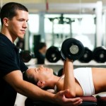 A male personal trainer spotting a female whilst performing dumbbell chest presses.