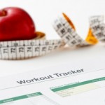 An apple and a tape measure next to a workout tracker sheet.