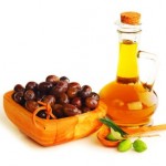 A wooden bowl of black olives next to a bottle of extra virgin olive oil.