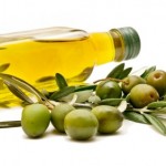 A bottle of olive oil on it's side next to a branch of green olives.