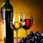 A bottle of wine, 2 glasses of wine and a pile of grapes.