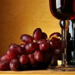 A bunch of red grapes next to a glass and bottle of red wine.