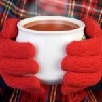 A woman with gloves holding a bowl of hot tomato soup.
