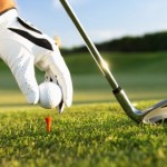 A close up shot of a golf ball being placed on a tee and a golf club.