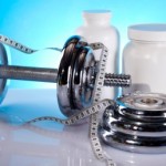 A set of dumbbells and weight plates next to some white bottles of fat burners.