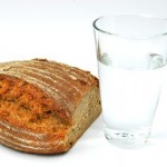 A loaf of wholegrain bread next to a glass of water.