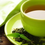 A cup of green tea on a green saucer with green tea leaves.