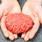 A person holding a home made burger patty in their hand.