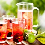 A jug and three glasses of berry infused lemonade on an outdoor table.