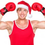 A man in a Santa hat flexing his muscles and wearing boxing gloves.