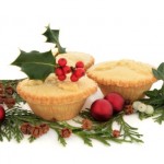 Three mince pies surrounded by baubles and holly.