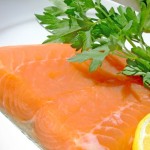 A close up shot of a salmon fillet garnished with lemon and parsley.