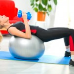 Woman doing fitness exercises with dumbbells and ball at home